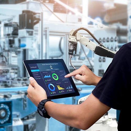 person in a factory holding a tablet displaying a smart manufacturing dashboard